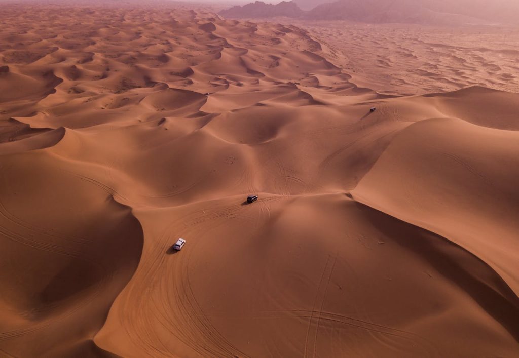 Stunning aerial capture of vehicles navigating expansive sand dunes under the desert sun.